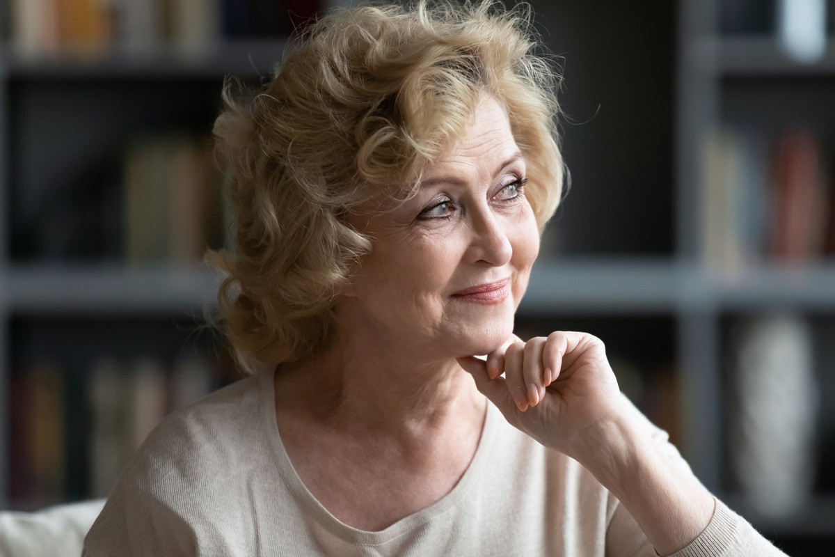 dojrzała kobieta z blond lokami patrzy zalotnie w dal rozmarzonym wzrokiem