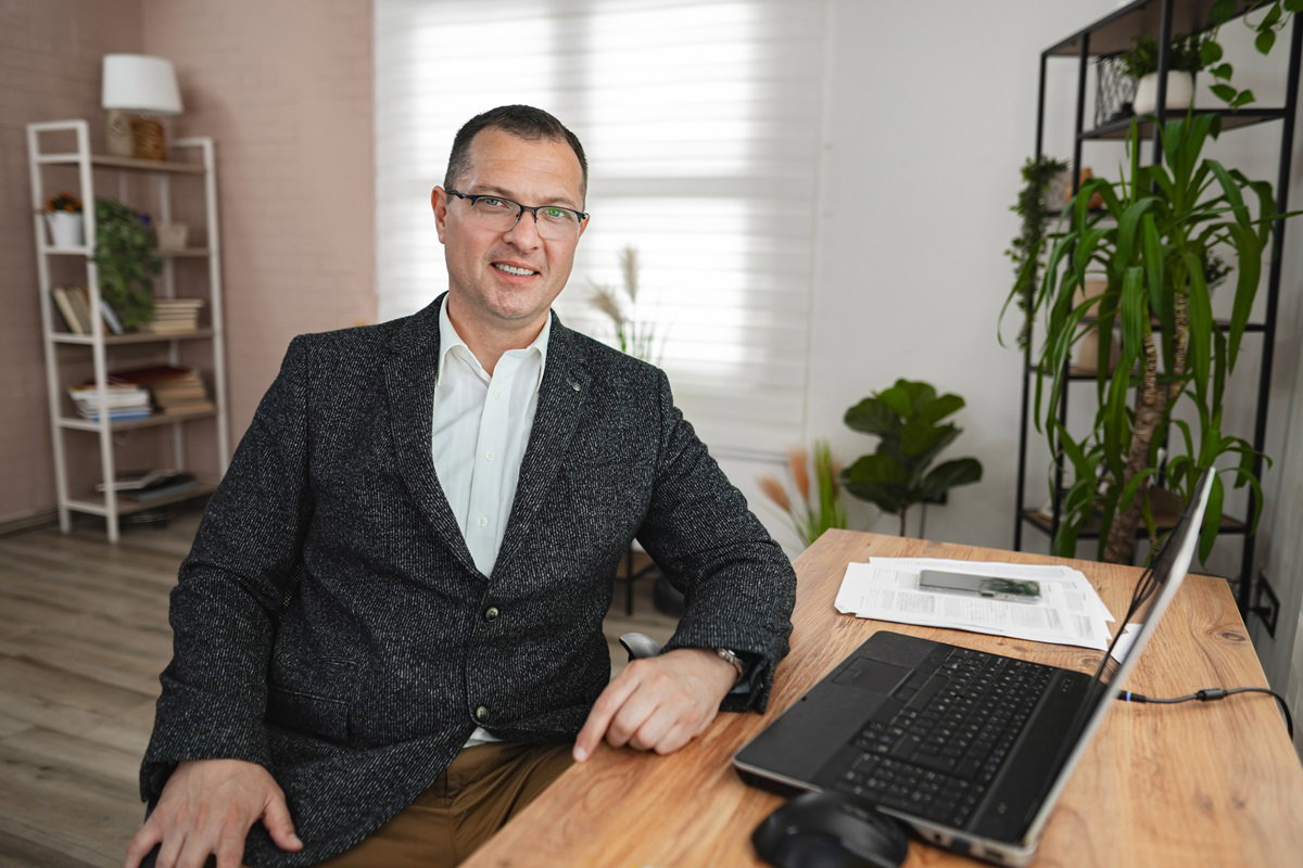 Professional man in gray blazer sitting at a desk with laptop in a cozy home office setting during the daytime