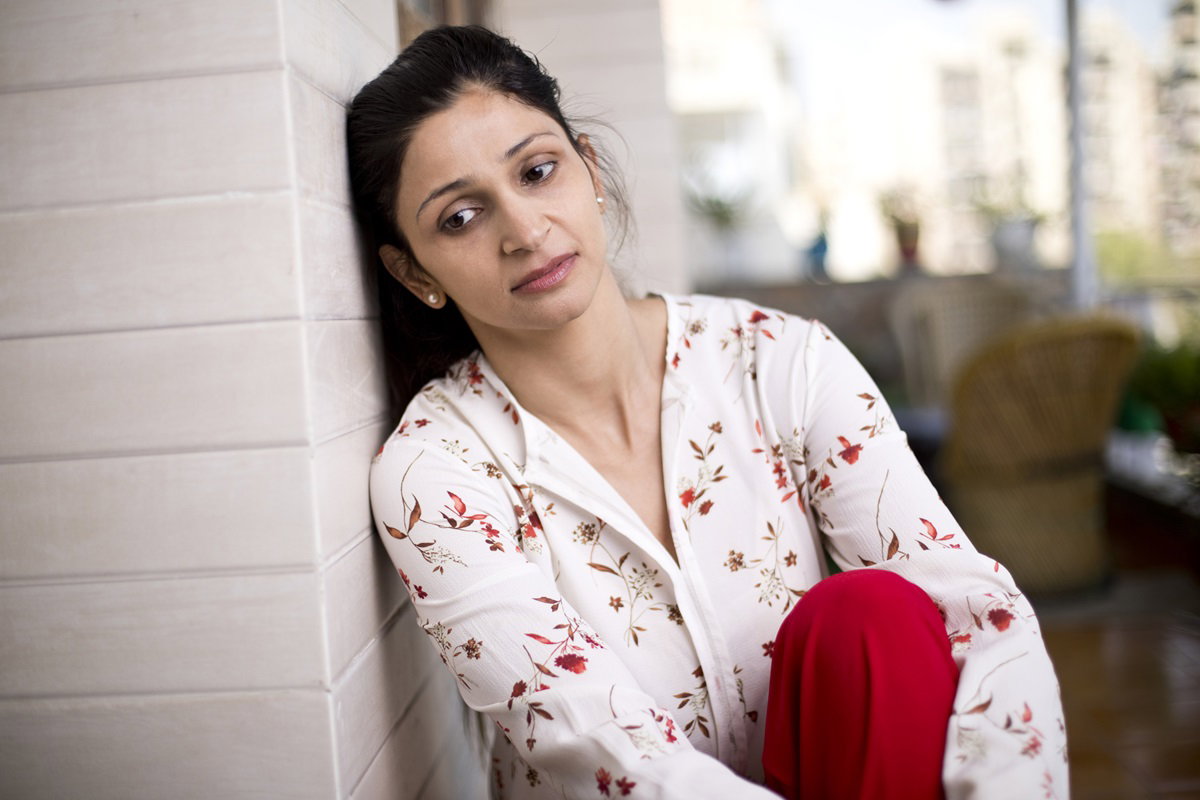 młoda dziewczyna w bluzce w czerwone kwiaty i listki oparta o ścianę rozmyśla