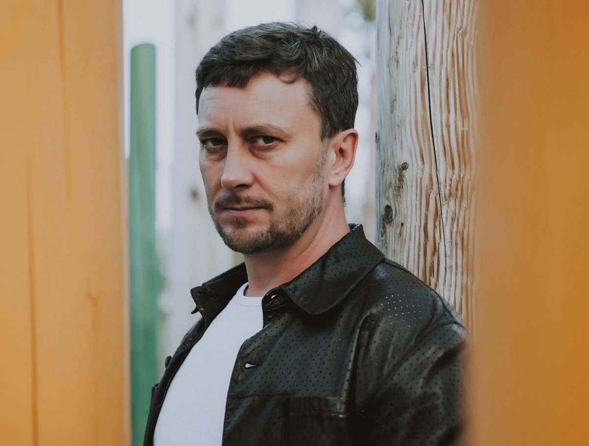 mężczyzna w średnim wieku stoi na dworze w skórzanej kurtce i smutno patrzy przed siebie