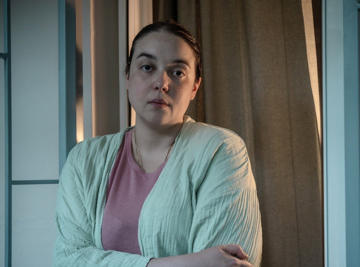 kobieta w średnim wieku z ciemnymi włosami w jasnozielonym szlafroku i różowej bluzce patrzy zrezygnowana przed siebie