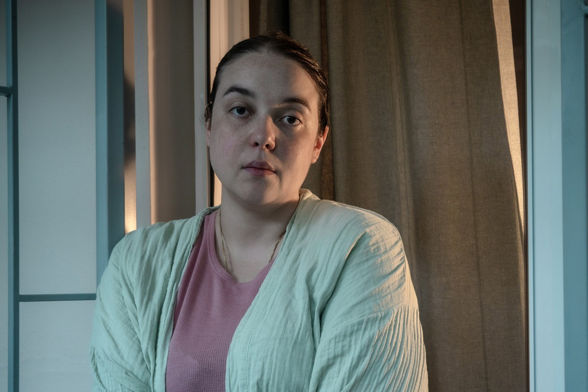 kobieta w średnim wieku z ciemnymi włosami w jasnozielonym szlafroku i różowej bluzce patrzy zrezygnowana przed siebie