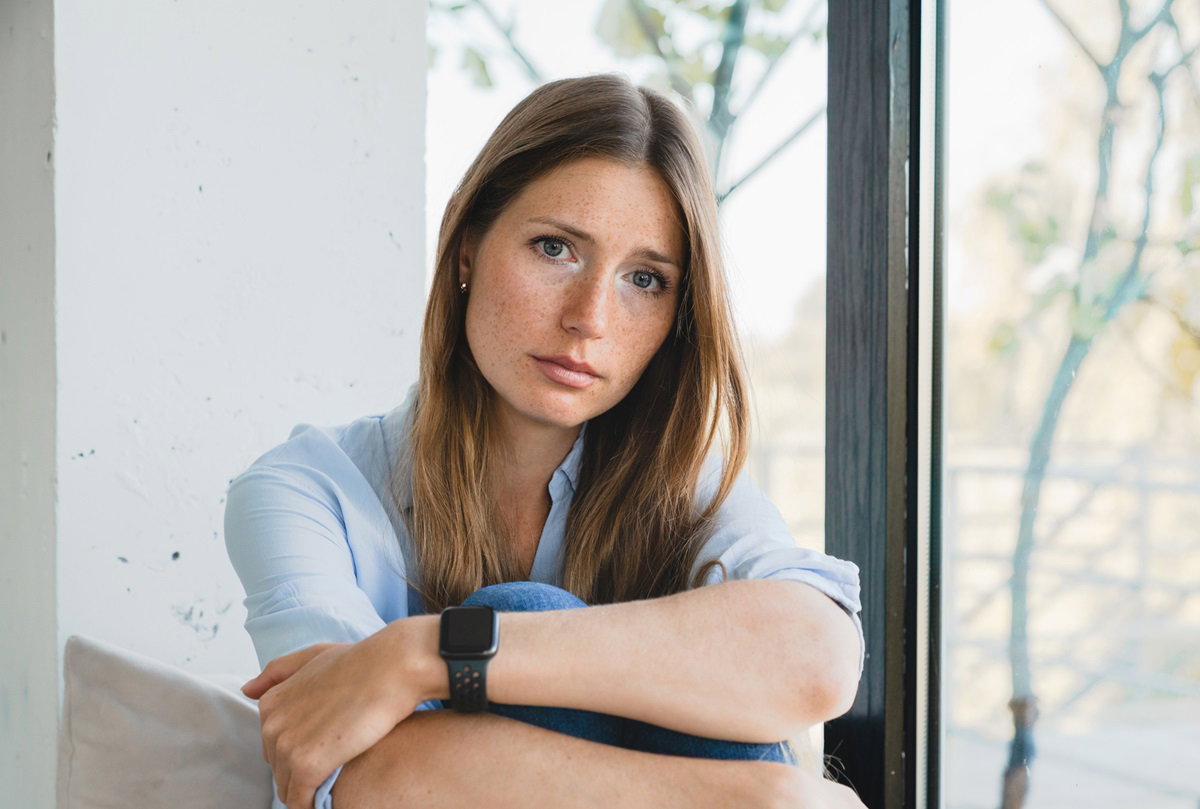 smutna dziewczyna z piegami siedzi skulona przy oknie