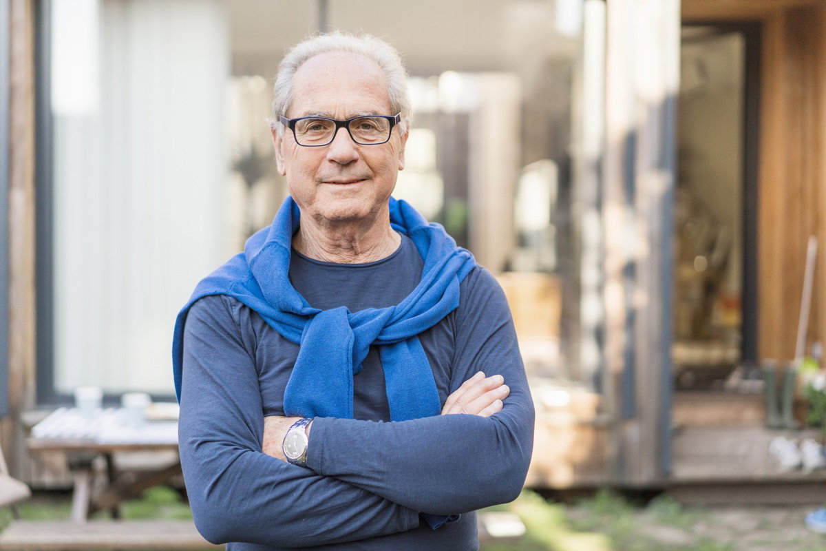 mężczyzna senior w okularach pewny siebie z lekkim uśmiechem stoi na działce