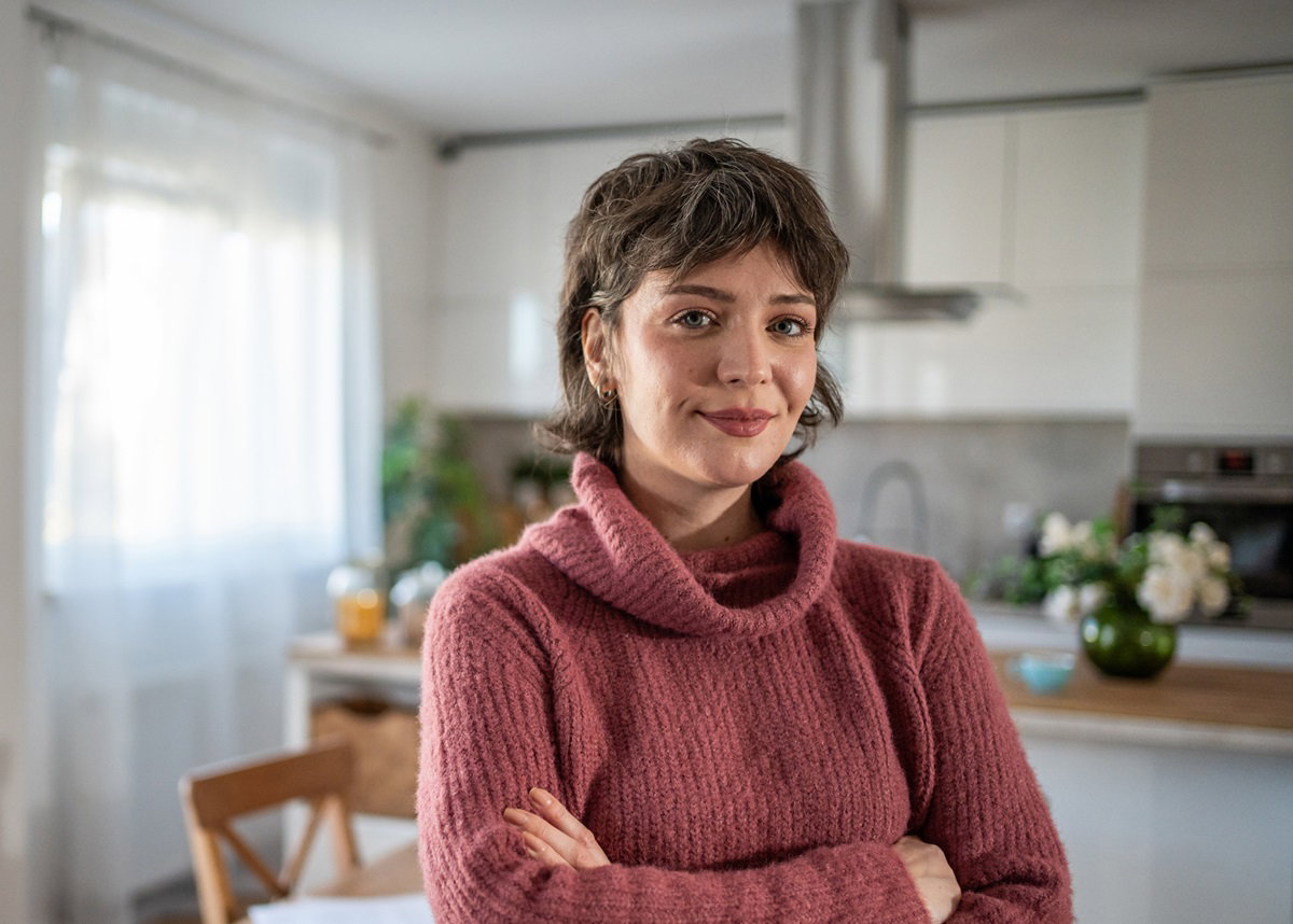mloda kobieta z krótkimi włosami stoi w kuchni z założonymi rękami i lekko się uśmiecha