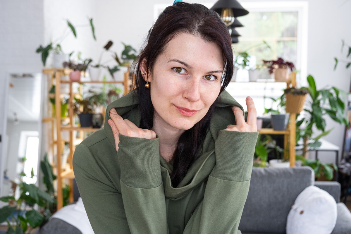 młoda kobieta w zielonej bluzie z kapturem patrzy przed siebie z lekkim uśmiechem