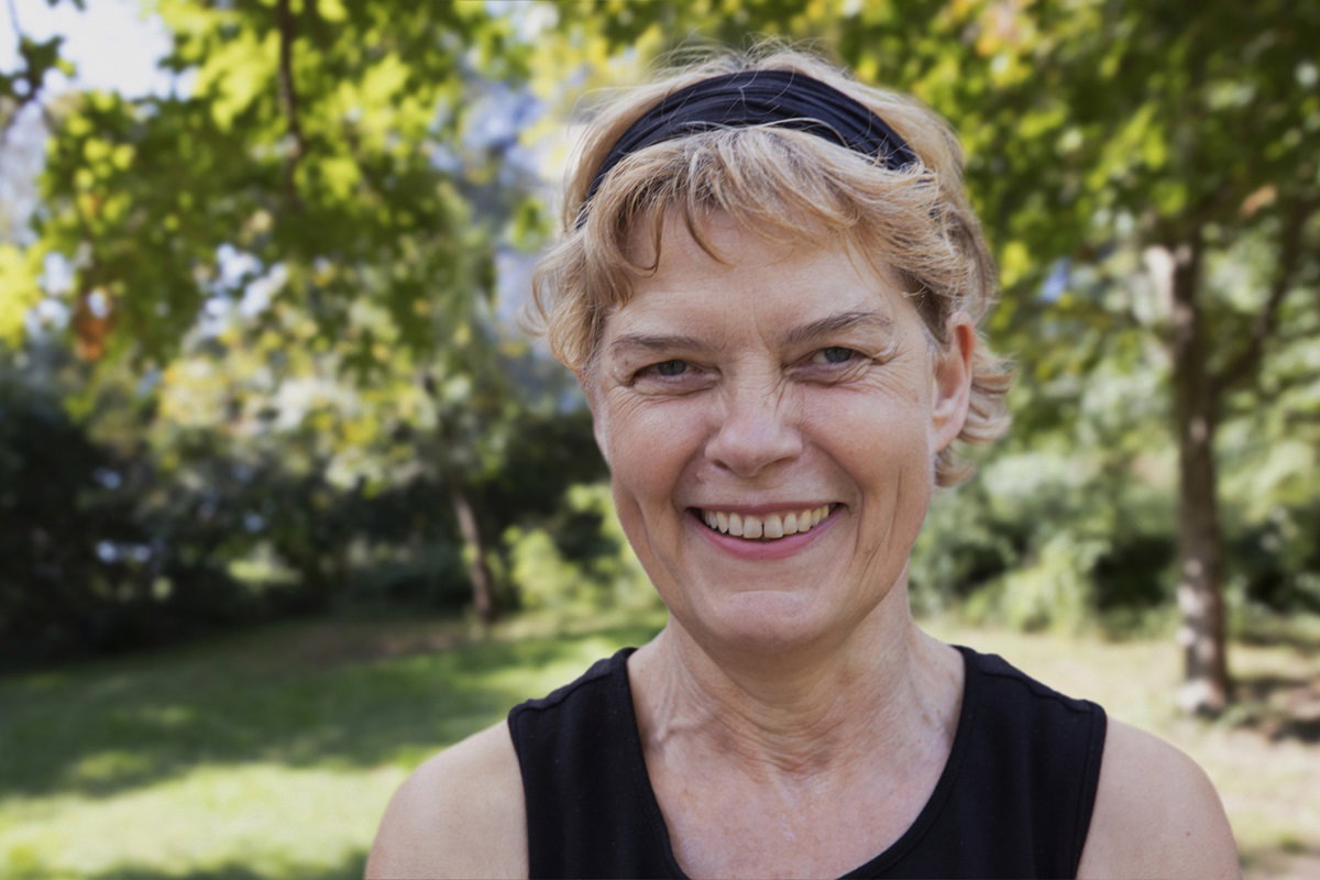 kobieta  w dojrzałym wieku szeroko się uśmiecha stojąc na świeżym powietrzu