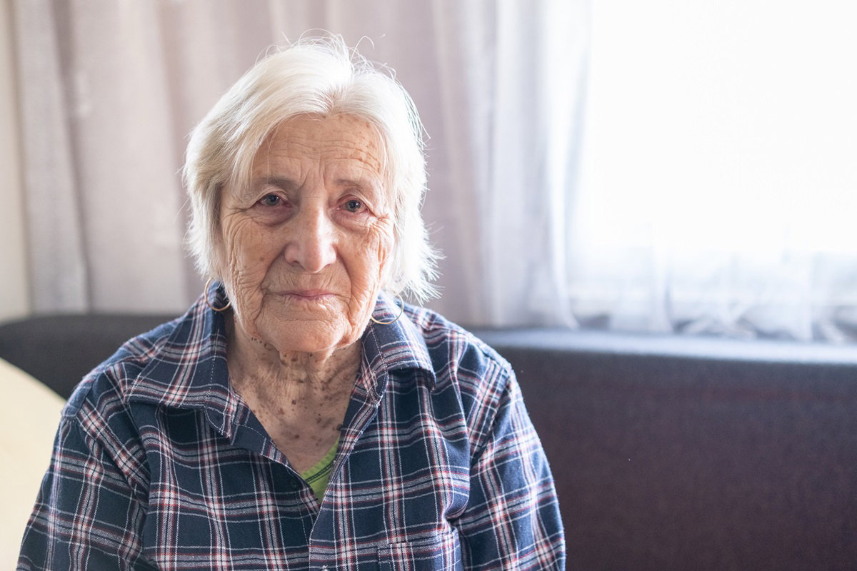 starsza kobieta z krótkimi siwymi włosami patrzy zmartwionym wzrokiem siedząc na kanapie