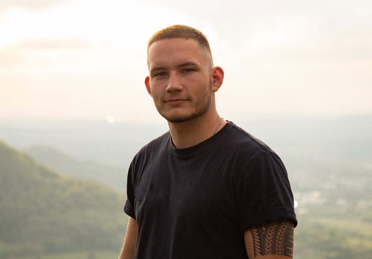 młody mężczyzna w czarnym t-shircie i z tatuażem na ramieniu patrzy z pewną siebie miną