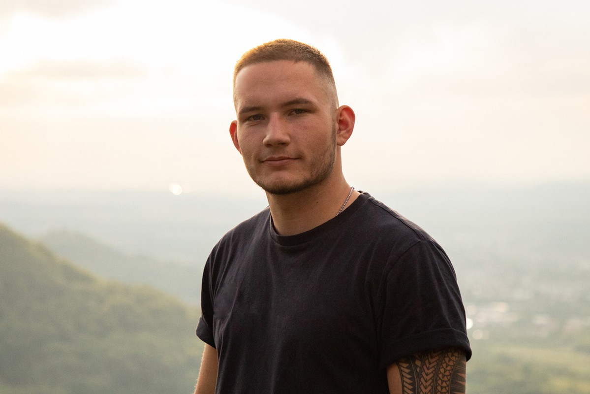 młody mężczyzna w czarnym t-shircie i z tatuażem na ramieniu patrzy z pewną siebie miną