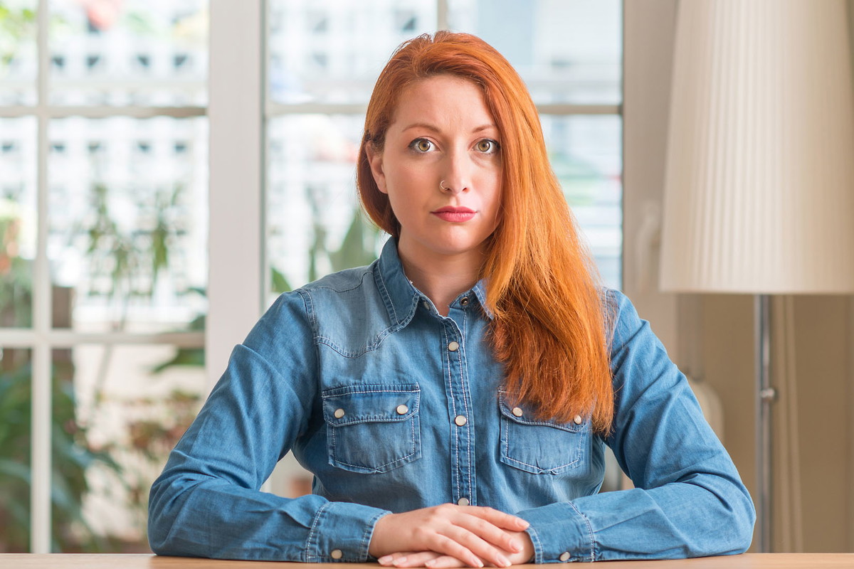 Redhead woman at home with serious expression on face. Simple and natural looking at the camera.