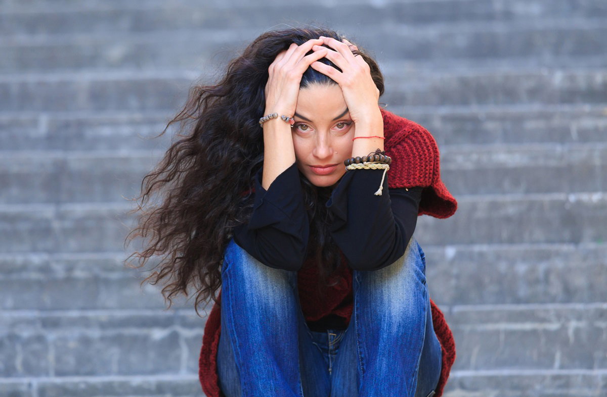 kobieta z długimi ciemnymi włosami siedzi na schodach z rękami na głowie