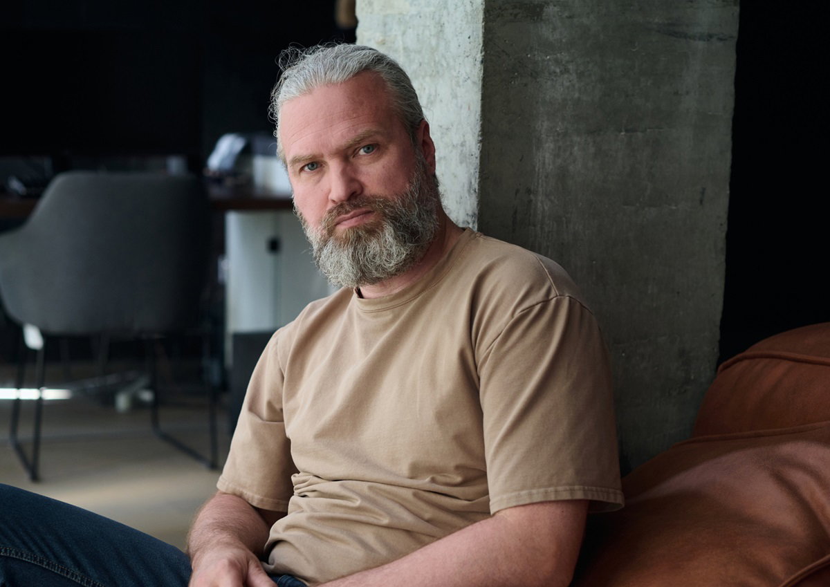 mężczyzna w dojrzałym wieku z siwą brodą siedzi na kanapie ze zrezygnowaną miną