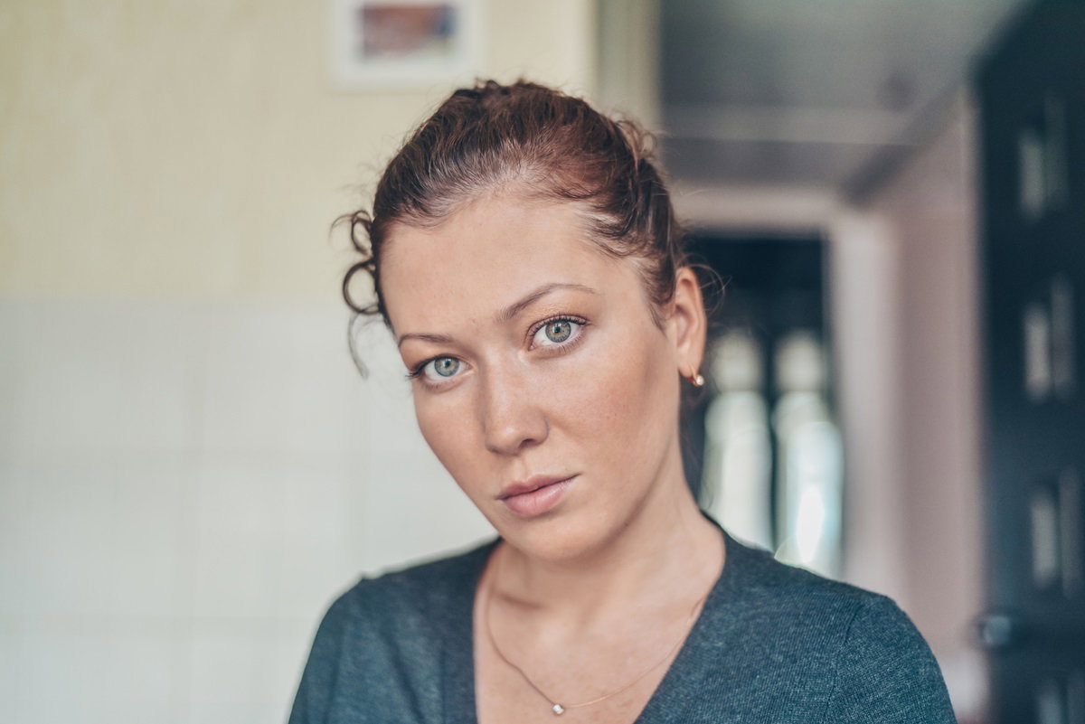 młoda kobieta ze spiętymi włosami i w szarym sweterku stoi i patrzy smutnym wzrokiem