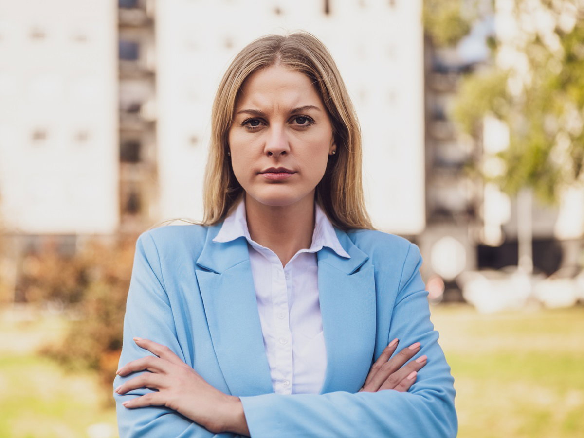 młoda kobieta z długimi blond włosami stoi ze zdeterminowaną miną i założonymi rękami