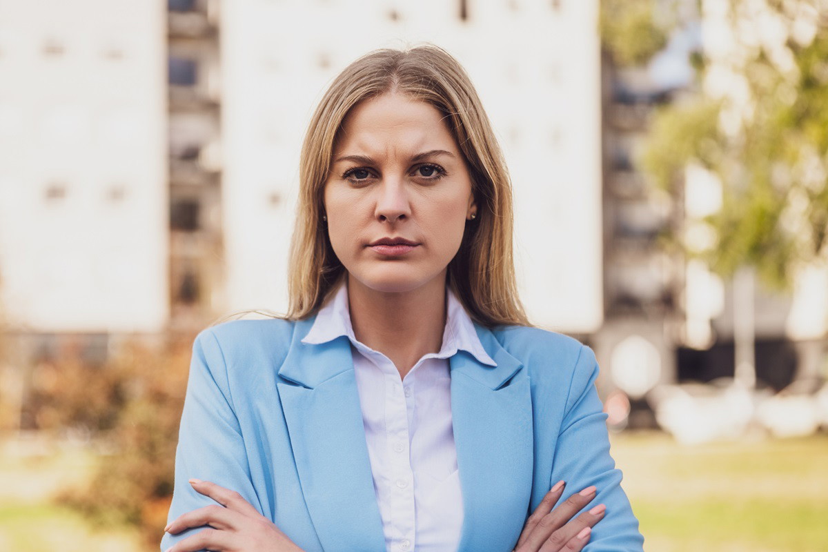 młoda kobieta z długimi blond włosami stoi ze zdeterminowaną miną i założonymi rękami