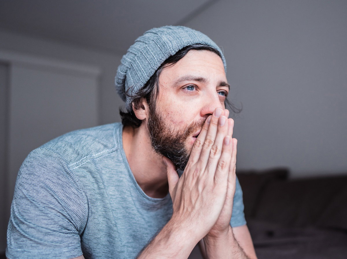 młody mężczyzna z brodą i w czapce siedzi ze złożonymi dłońmi ze zrozpaczoną miną