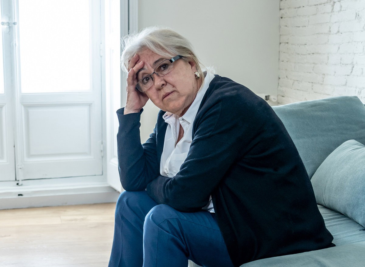 starsza kobieta w senioralnym wieku z siwymi włosami siedzi na kanapie i patrzy z dezaprobatą