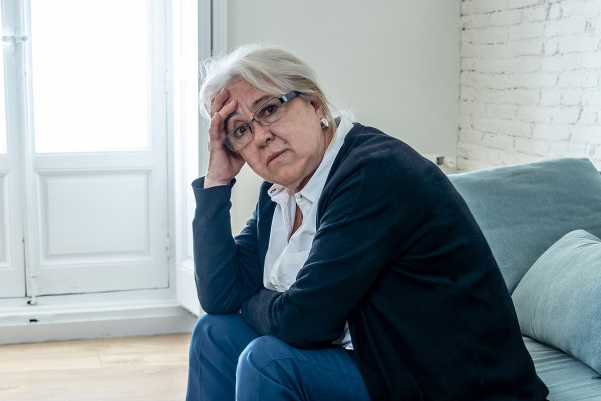 starsza kobieta w senioralnym wieku z siwymi włosami siedzi na kanapie i patrzy z dezaprobatą