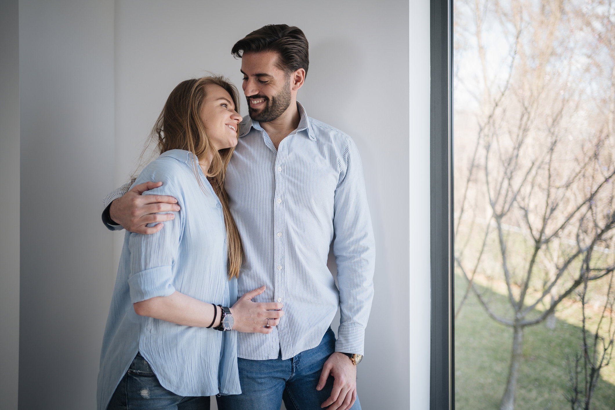 Happy young couple in bedroom looking out sunny window