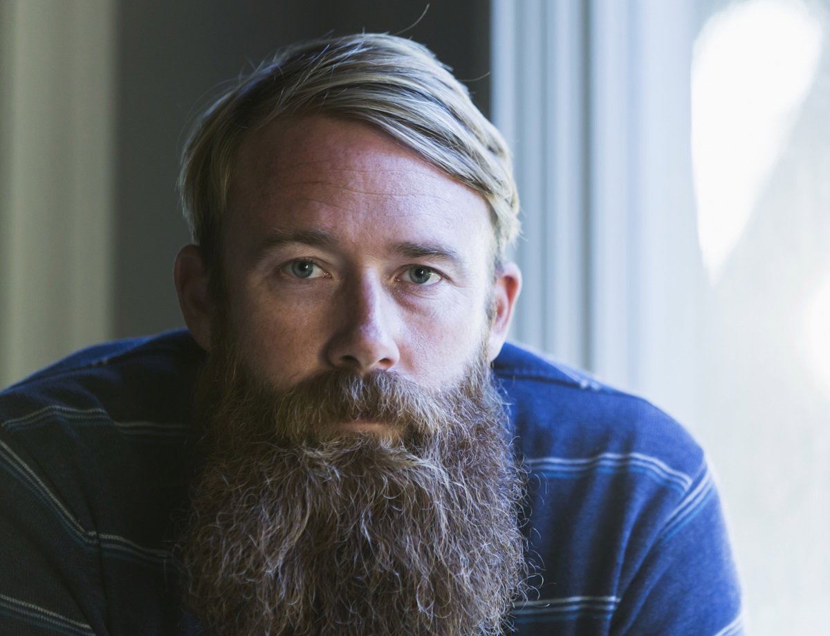 mężczyzna w sile wieku z blond włosami i długą bujną brodą patrzy przed siebie smutnym wzrokiem