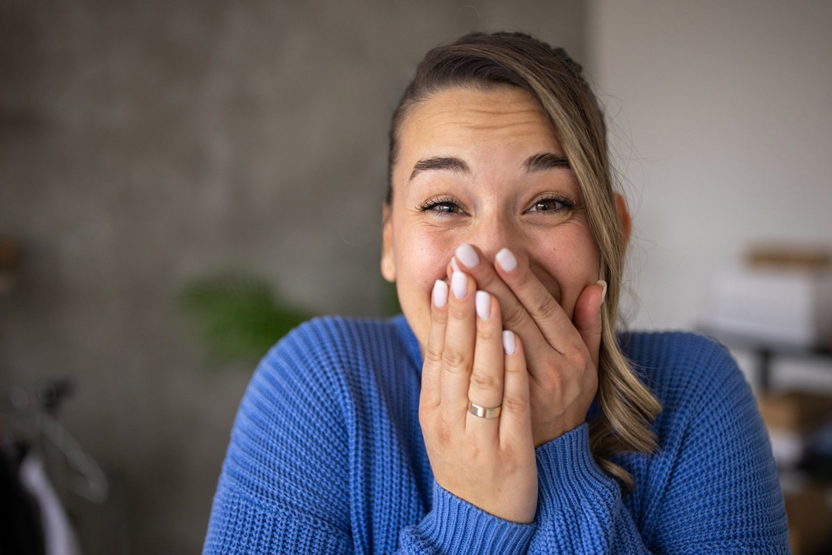 młoda kobieta w niebieskim swetrze z rękami przy ustach jest zszokowana