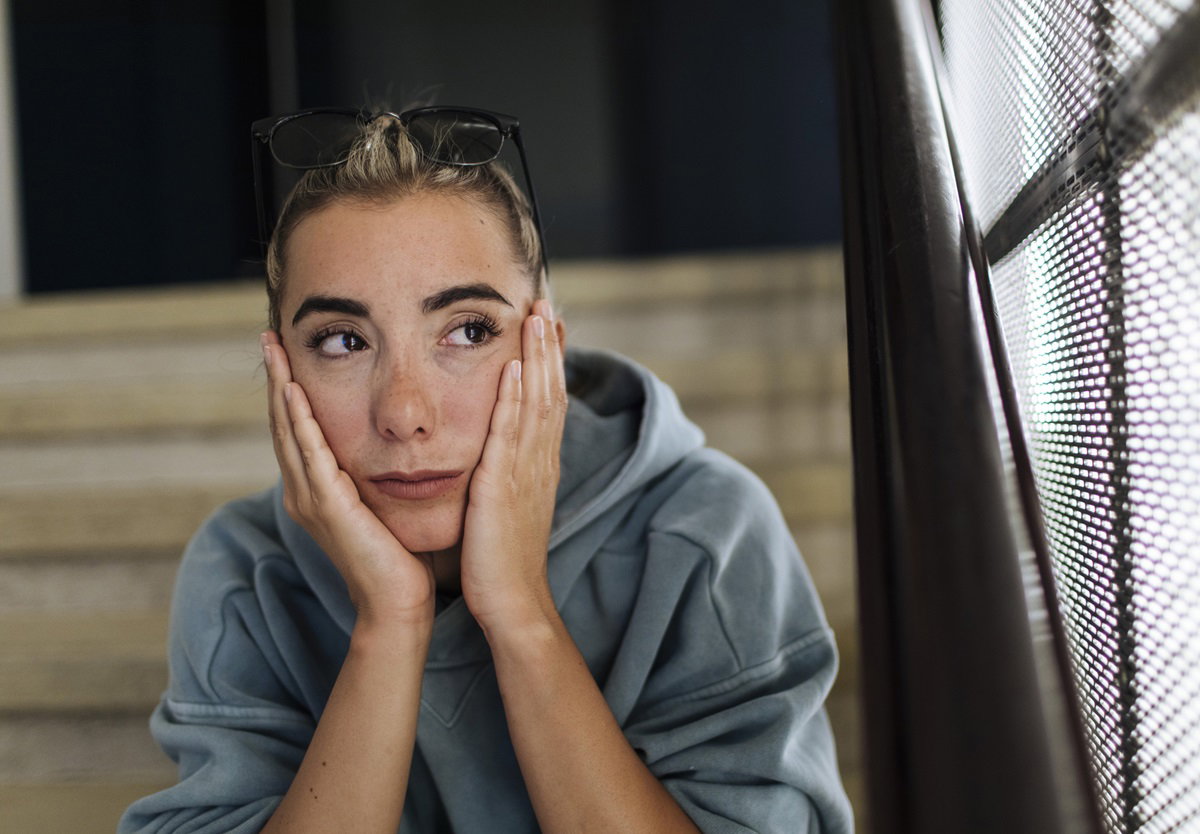 młoda kobieta w bluzie z kapturem siedzi na schodach z głową w dłoniach i patrzy smutnym wzrokiem