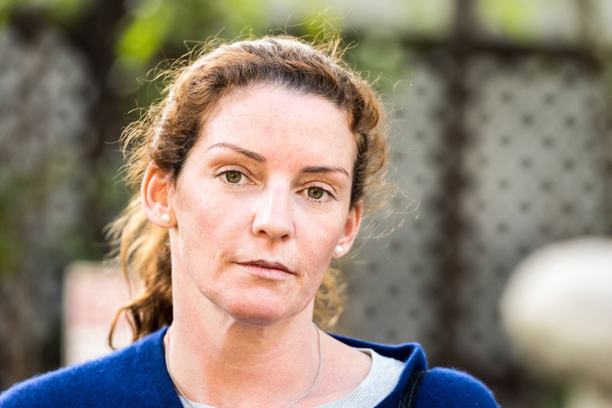 kobieta w średnim wieku z rudymi kręconymi włosami patrzy przed siebie poważnym wzrokiem