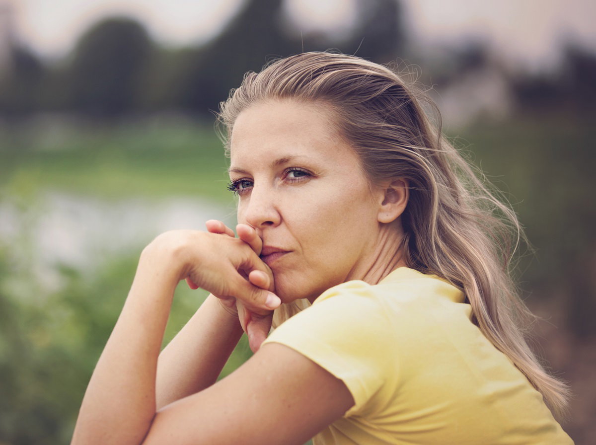 młoda kobieta w żółtym t-shircie siedzi nad jeziorem i patrzy zamyślona w dal