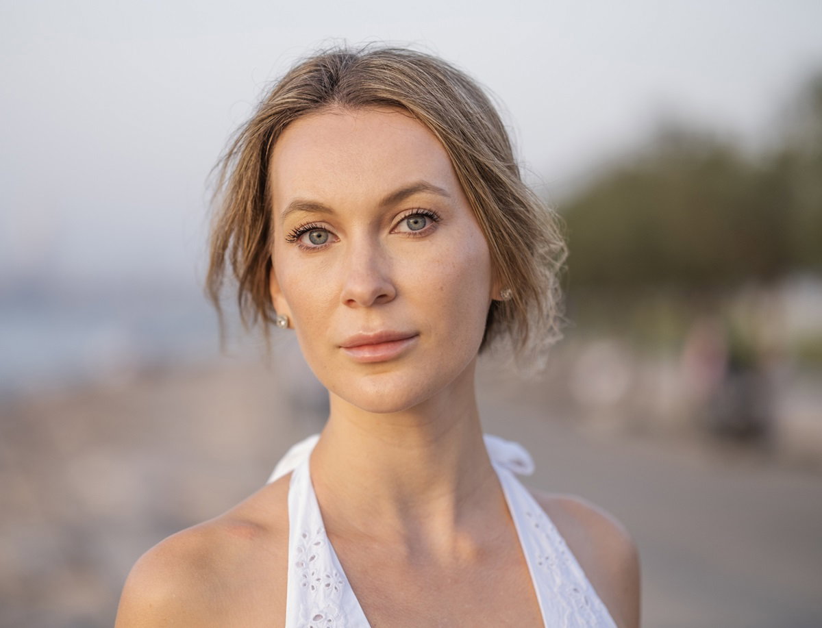 młoda kobieta z blond włosami i w białej sukience na plaży patrzy przed siebie smutnym wzrokiem