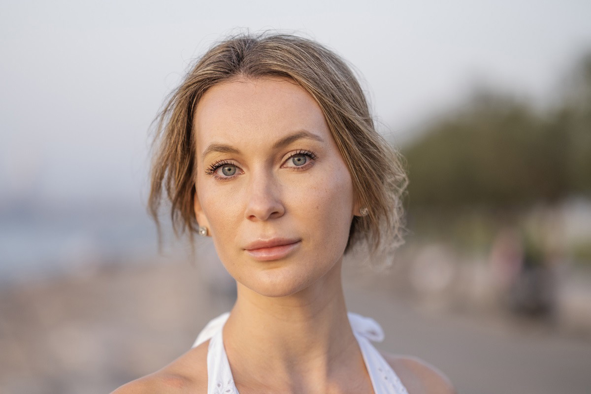 młoda kobieta z blond włosami i w białej sukience na plaży patrzy przed siebie smutnym wzrokiem