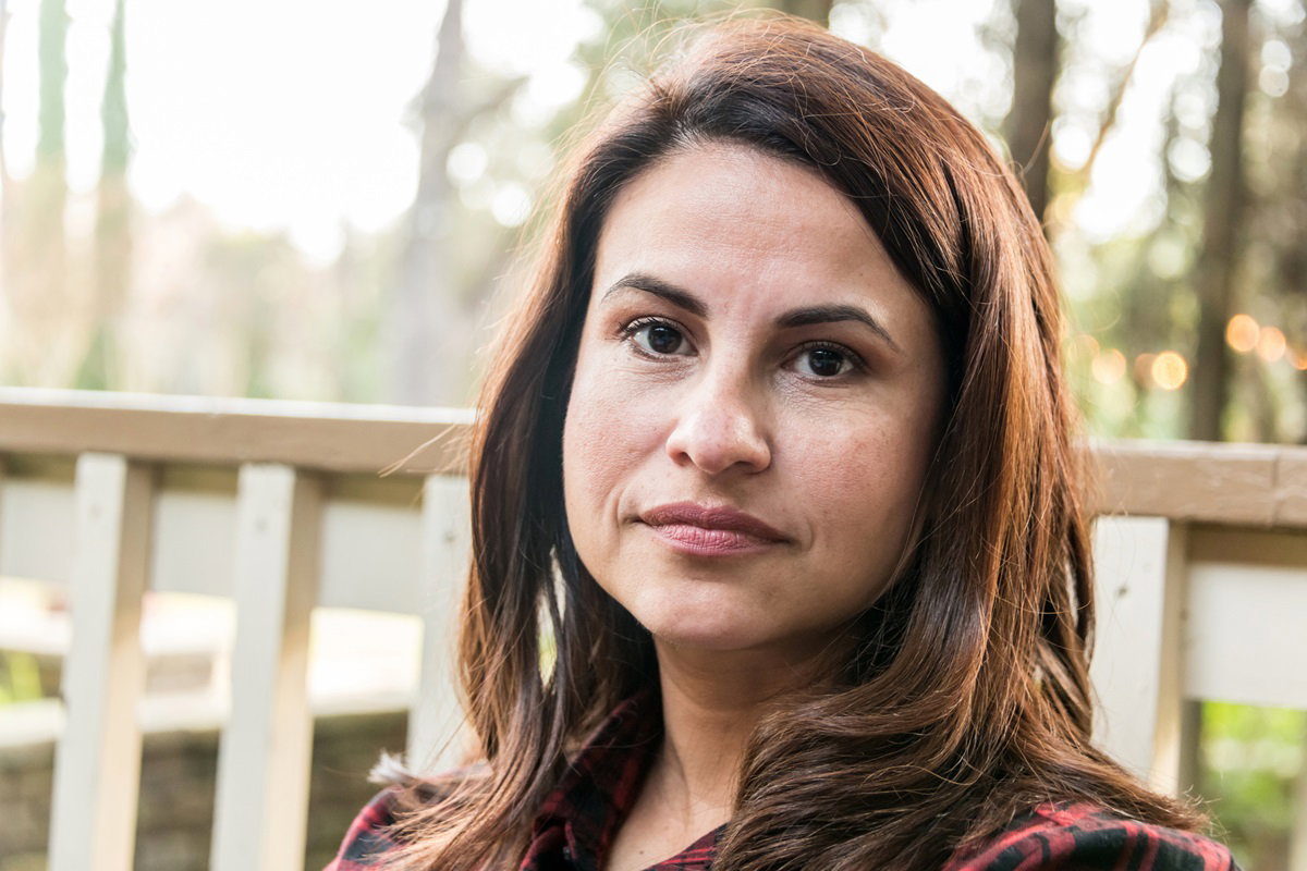 kobieta w średnim wieku z brązowymi oczami i włosami siedzi na zewnątrz i ma poważne spojrzenie