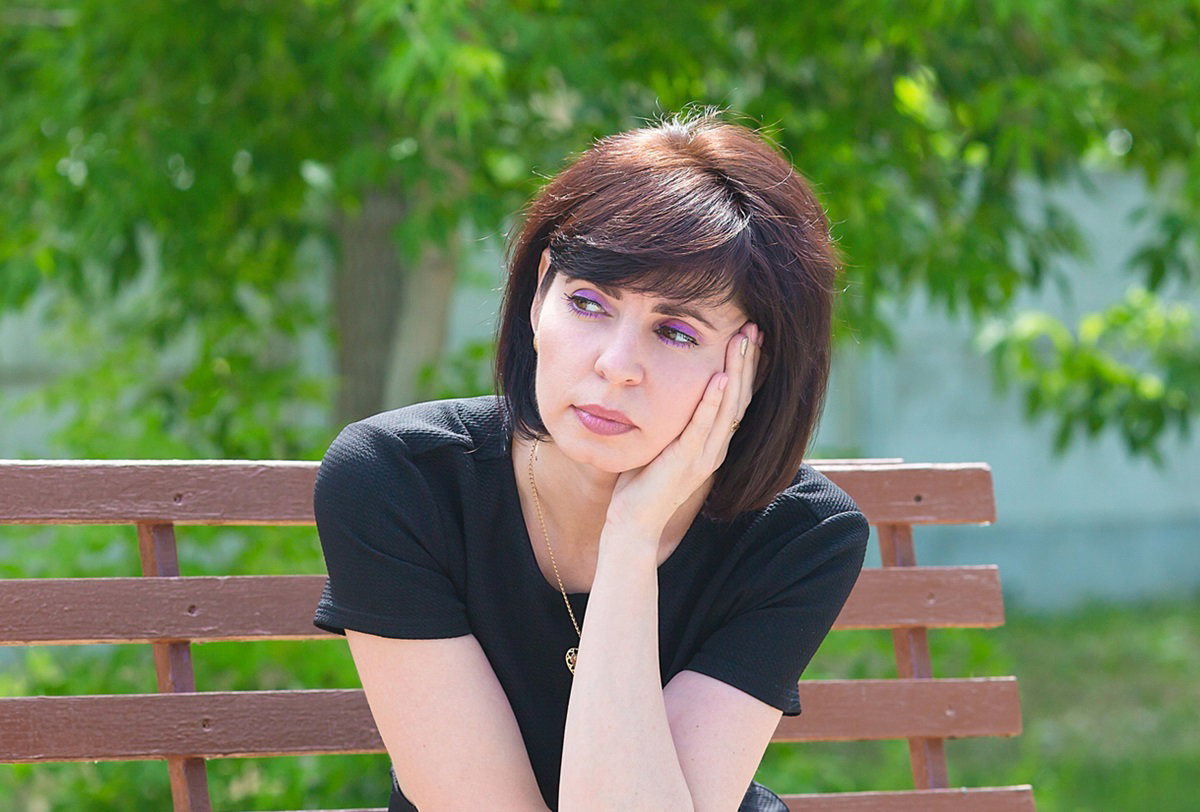 brunetka w średnim wieku w czarnej sukience siedzi na ławce i rozmyśla rozgoryczona