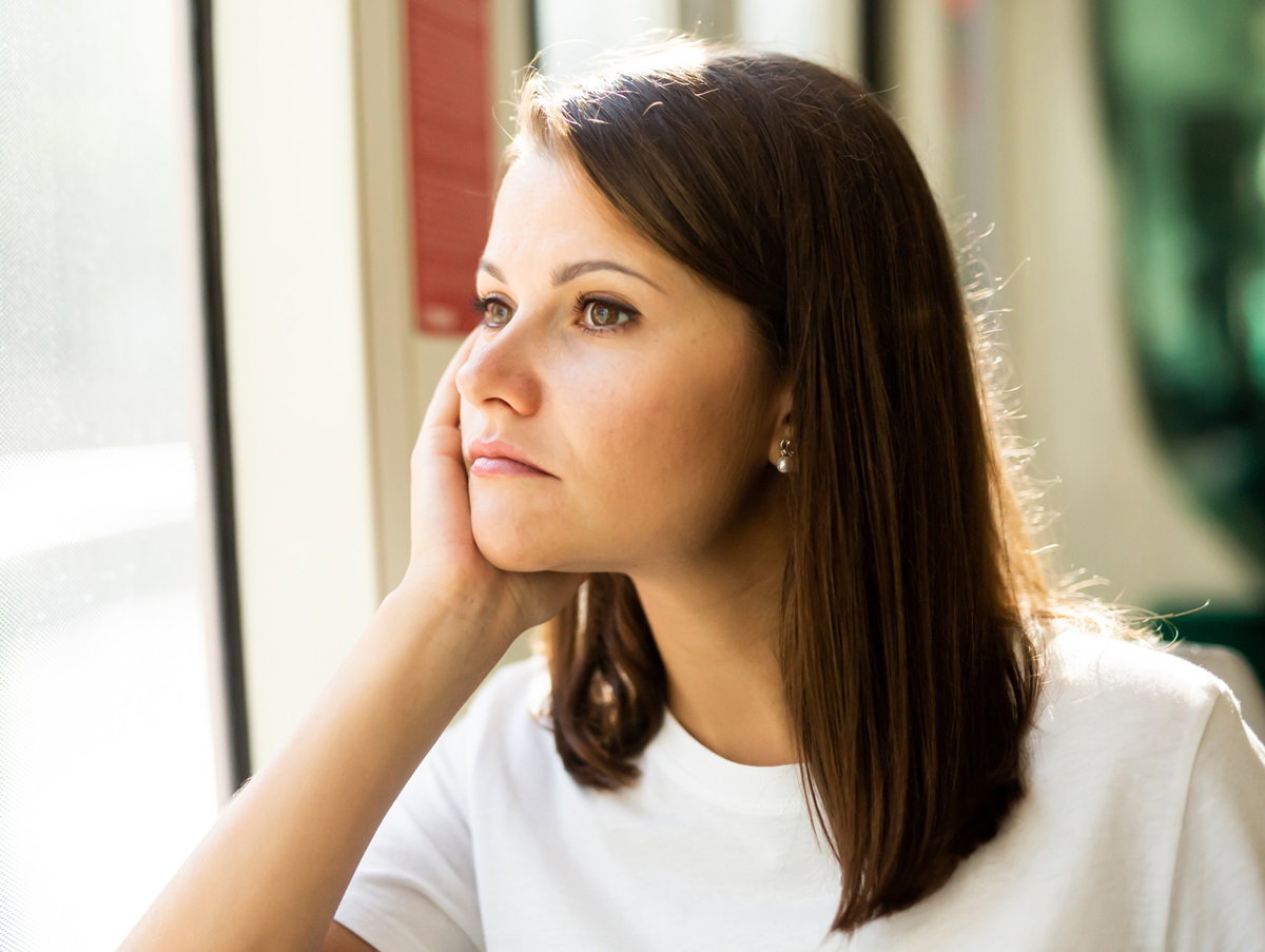 młoda dziewczyna z ciemnymi włosami patrzy w okno zamyślona i smutna