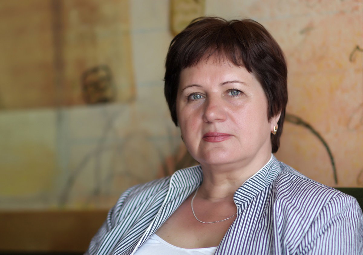 kobieta w dojrzałym wieku z krótkimi włosami siedzi na fotelu i patrzy poważnym wzrokiem