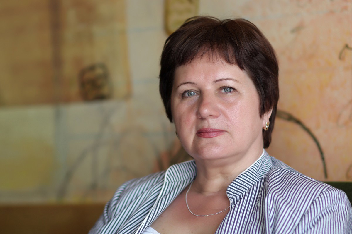 kobieta w dojrzałym wieku z krótkimi włosami siedzi na fotelu i patrzy poważnym wzrokiem