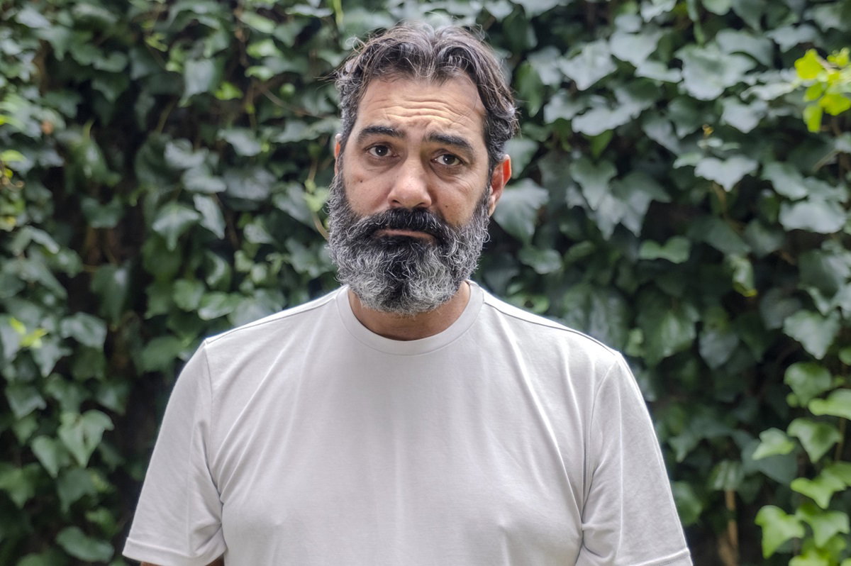 mężczyzna z brodą w średnim wieku na tle bluszczu patrzy zmartwionym wzrokiem