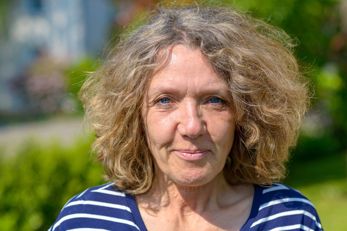 kobieta w dojrzałym wieku z burzą falowanych włosów stoi na dworze i się uśmiecha patrząc przed siebie