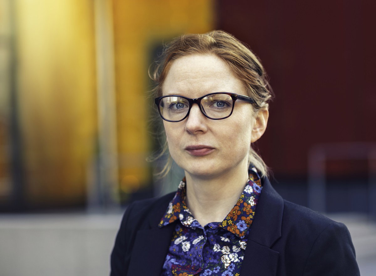 kobieta w okularach ze spiętymi włosami i w koszuli w kwiatki stoi na zewnątrz biura i patrzy poważnym wzrokiem