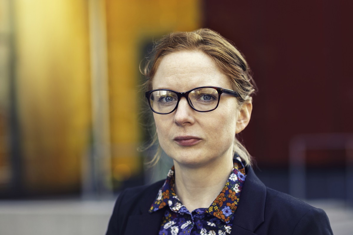 kobieta w okularach ze spiętymi włosami i w koszuli w kwiatki stoi na zewnątrz biura i patrzy poważnym wzrokiem