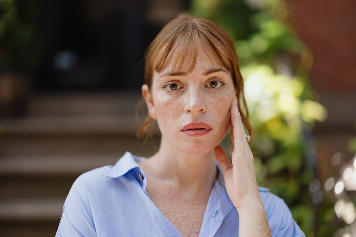 młoda kobieta z rudymi włosami i piegami stoi na zewnątrz i patrzy smutnym spojrzeniem