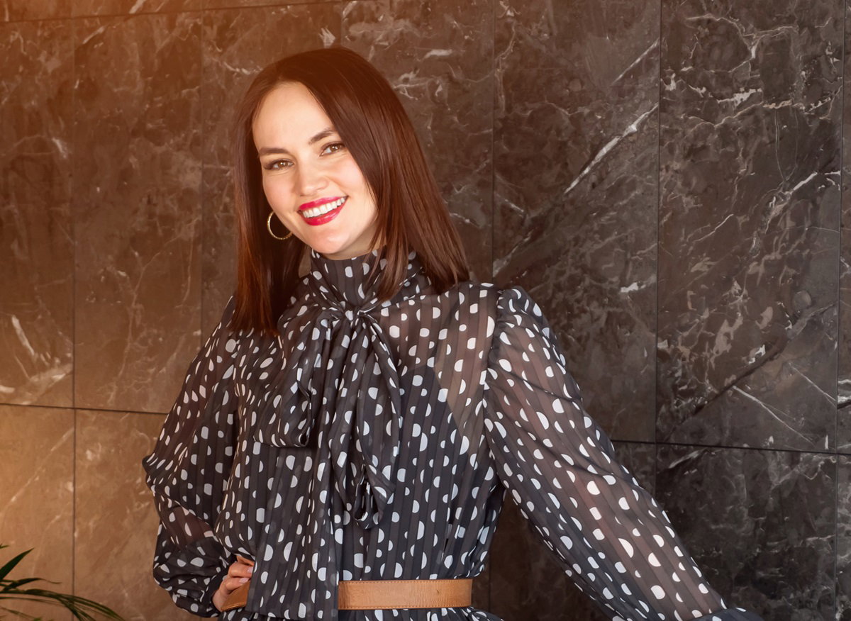 młoda kobieta w sukience w groszki uśmiecha się patrząc przed siebie