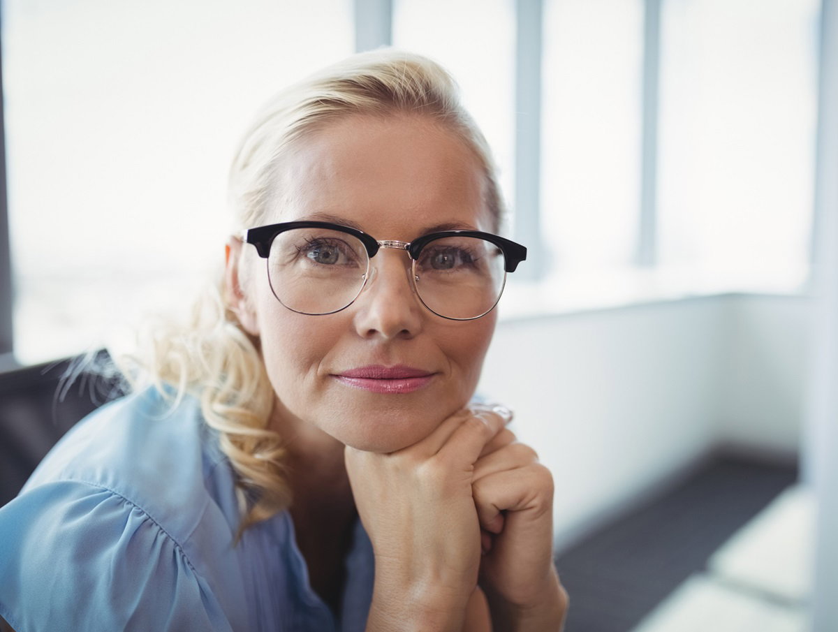 kobieta w średnim wieku z jasnymi włosami i w okularach siedzi i patrzy z radością