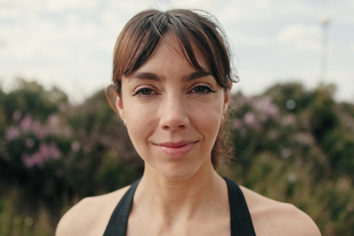 młoda kobieta w spiętych włosach i kostiumie kąpielowym stoi na zewnątrz i lekko się uśmiecha zamyślona