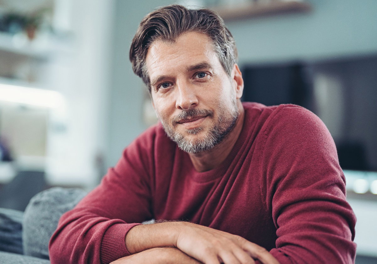 mężczyzna w średnim wieku w czerwonym swetrze siedzi na kanapie i patrzy zamyślonym wzrokiem