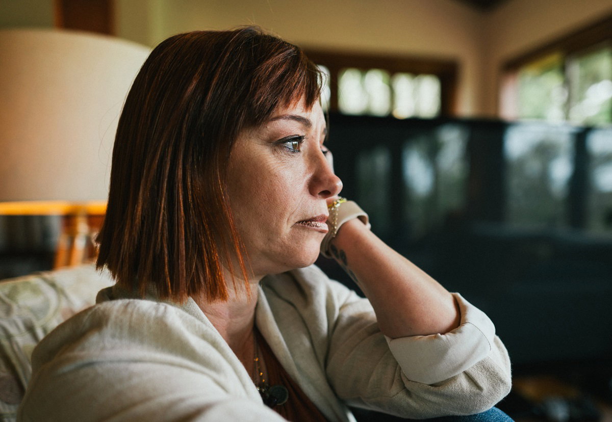 zrozpaczona kobieta z rudymi włosami siedzi na kanapie i rozmyśla patrząc w dal