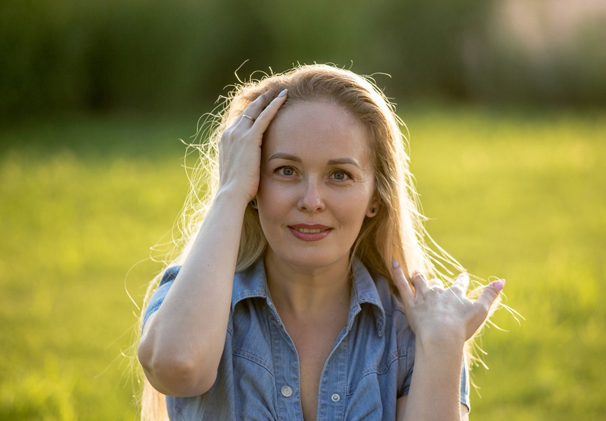 kobieta w średnim wieku blondynka w jeansowej sukience stoi na świeżym powietrzu i lekko się uśmiecha