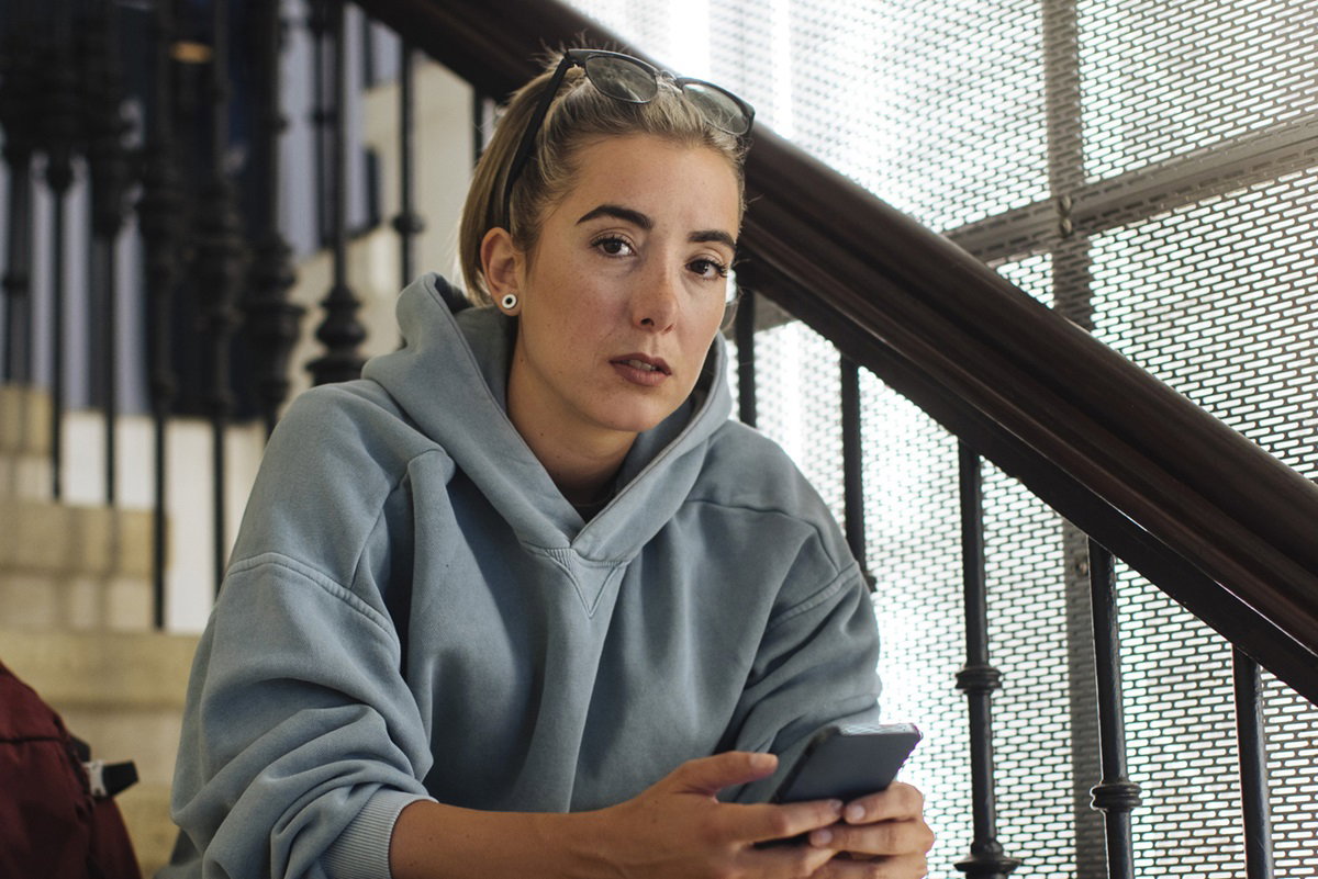 młoda kobieta siedzi na schodach z telefonem w ręku i patrzy rozgoryczonym wzrokiem