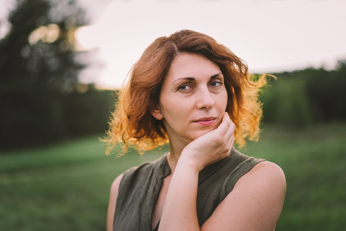 piękna dojrzała kobieta z kręconymi brązowo-rudymi włosami stoi na łonie natury i patrzy zamyślona