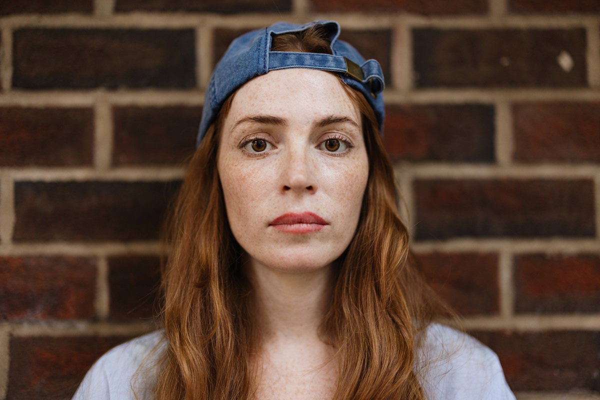 młoda kobieta o rudych długich włosach i w czapce z daszkiem założonej tył na przód patrzy przerażonym wzorkiem